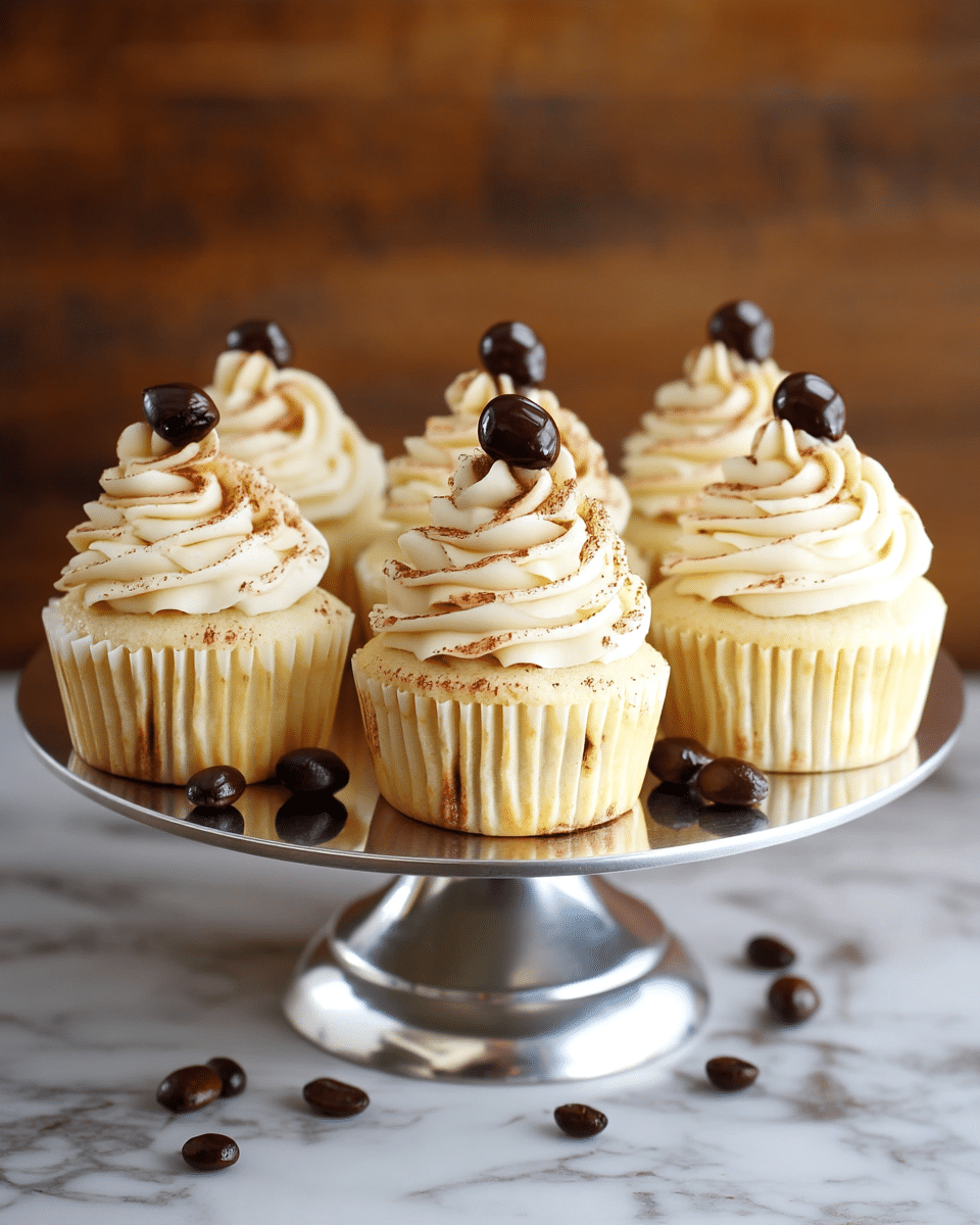 The image shows a close-up of a cupcake with three visible layers. The bottom layer is a golden brown cake with a soft crumb texture, visible from the bitten part. The middle layer is creamy white frosting with a smooth texture, and the top layer is a swirl of white frosting sprinkled lightly with cocoa powder, finishing with a shiny, dark brown chocolate-covered coffee bean at the peak. Behind it, there are more similarly decorated cupcakes on a white cake stand, all against a white marbled surface with a blurred neutral background. Photo taken with an iphone --ar 4:5 --v 7