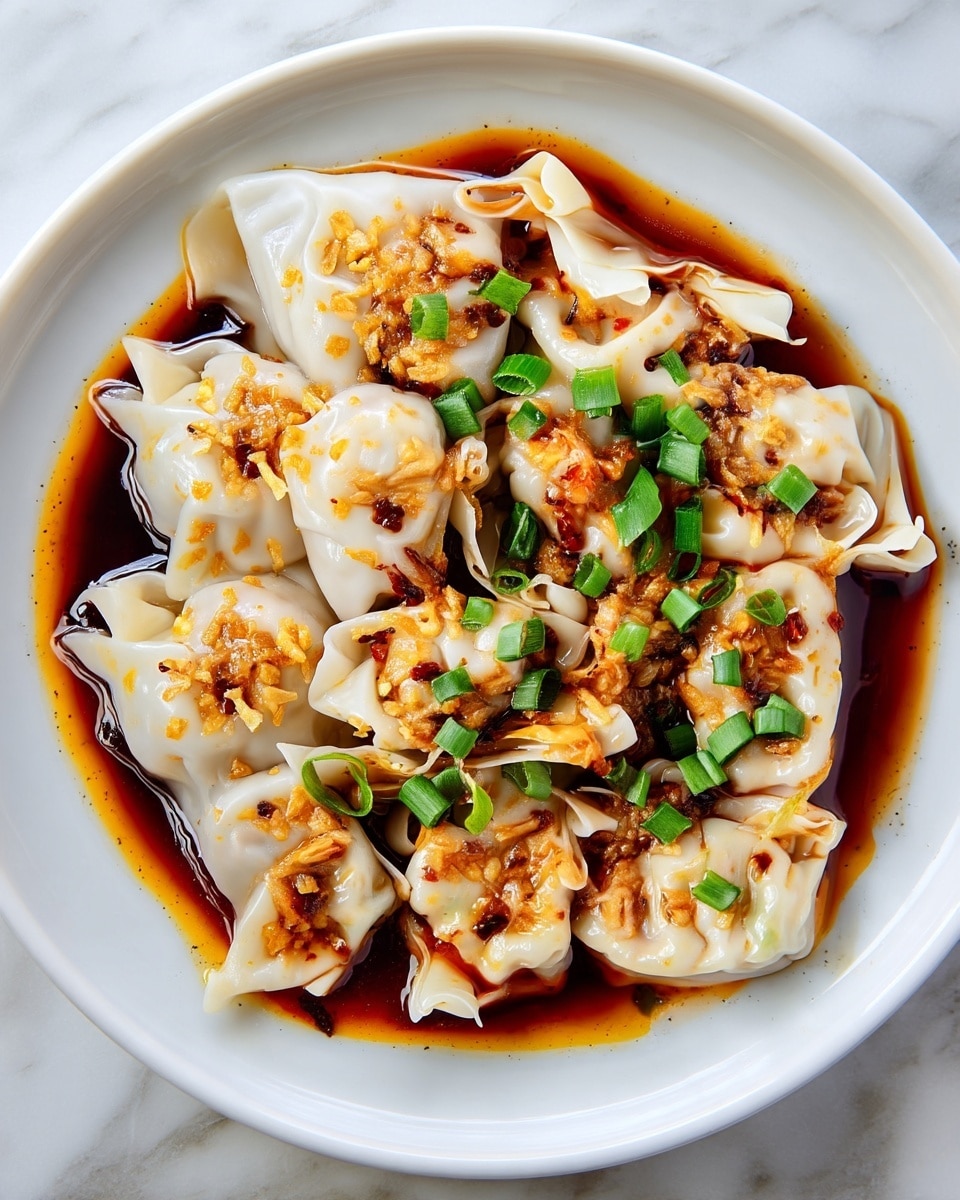 A close-up of a white plate filled with delicate wontons layered in a light, smooth skin with soft folds and edges, covered by a rich, dark brown chili oil sauce pooling around them. The wontons are topped with small bits of crispy fried garlic in golden brown color and scattered bright green chopped scallions, creating a contrast against the pale wonton skin and dark sauce. The texture of the wonton skin is slightly shiny and tender, with the sauce adding a glossy look on the edges. The entire dish is set on a white marbled surface. photo taken with an iphone --ar 4:5 --v 7