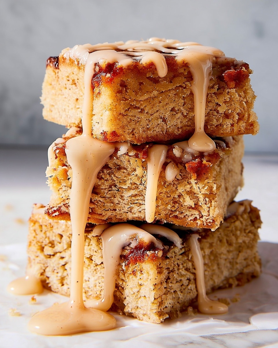 A stack of three thick, square blondie bars sits on a white marbled surface, each blondie showing a golden-brown, crumbly texture inside with slightly darker, caramelized edges. A smooth, light beige glaze is generously drizzled over the top blondie, slowly dripping down the sides and pooling at the base, enhancing the soft, moist appearance of the bars. The glaze adds a creamy contrast against the warm tones of the blondies, making the layers visually rich and inviting. Photo taken with an iphone --ar 4:5 --v 7
