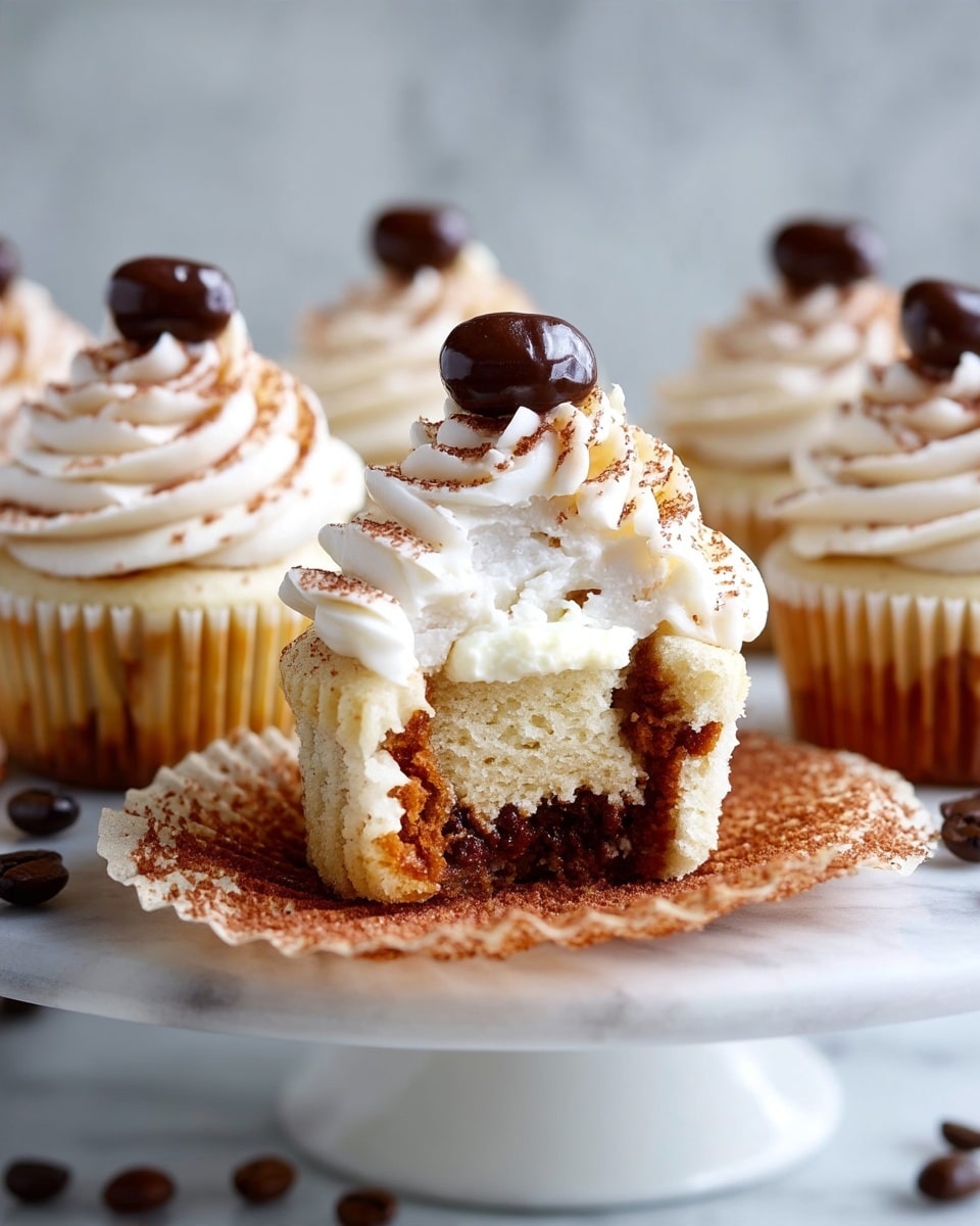Six vanilla cupcakes are arranged on a shiny silver cake stand. Each cupcake has a light yellow base with a white paper liner, topped with a tall swirl of creamy white frosting sprinkled lightly with brown powder. A glossy dark brown coffee bean sits on the peak of each frosting swirl. A few more dark brown coffee beans are scattered around the base of the cake stand. The background is a warm wooden texture with a white marbled surface below. photo taken with an iphone --ar 4:5 --v 7
